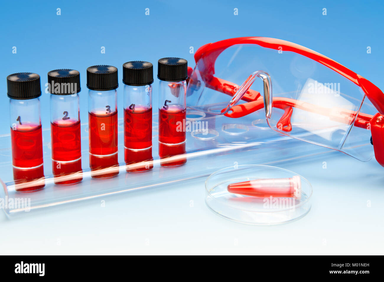 Tube stand full of samples, protective glasses and an automatic pipette on blue gradient background Stock Photo