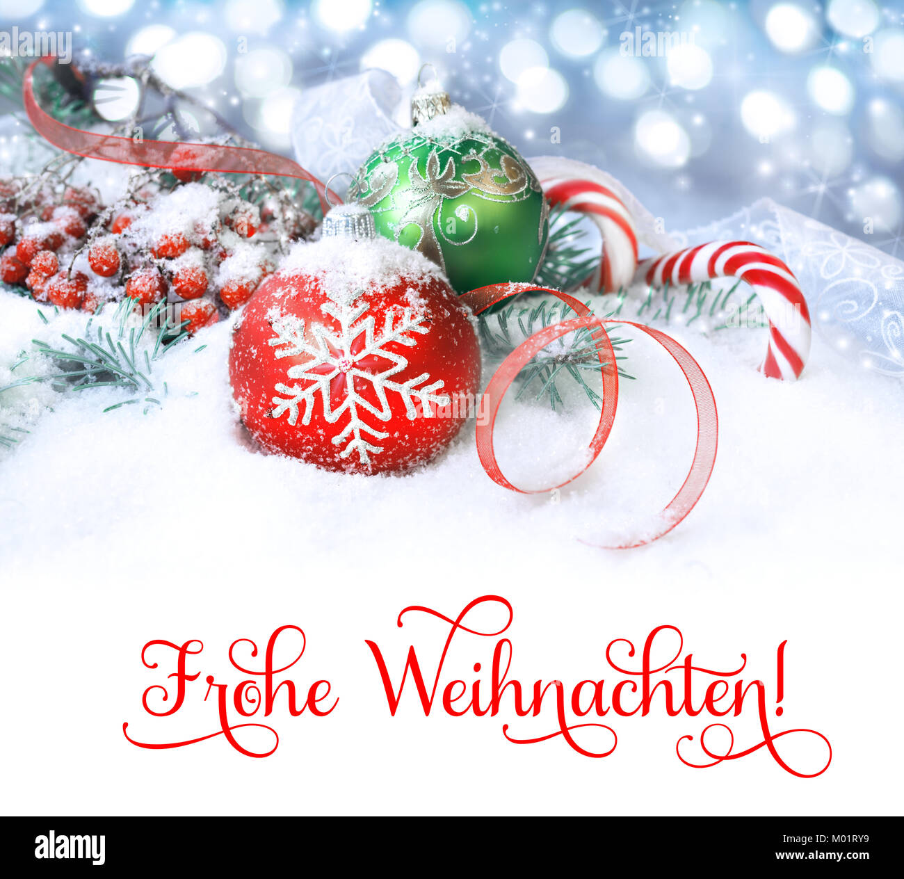 Red and green Christmas decorations on snow, isolated on white. Text 'Frohe Weihnachten'  can be replaced with your greeting. Stock Photo