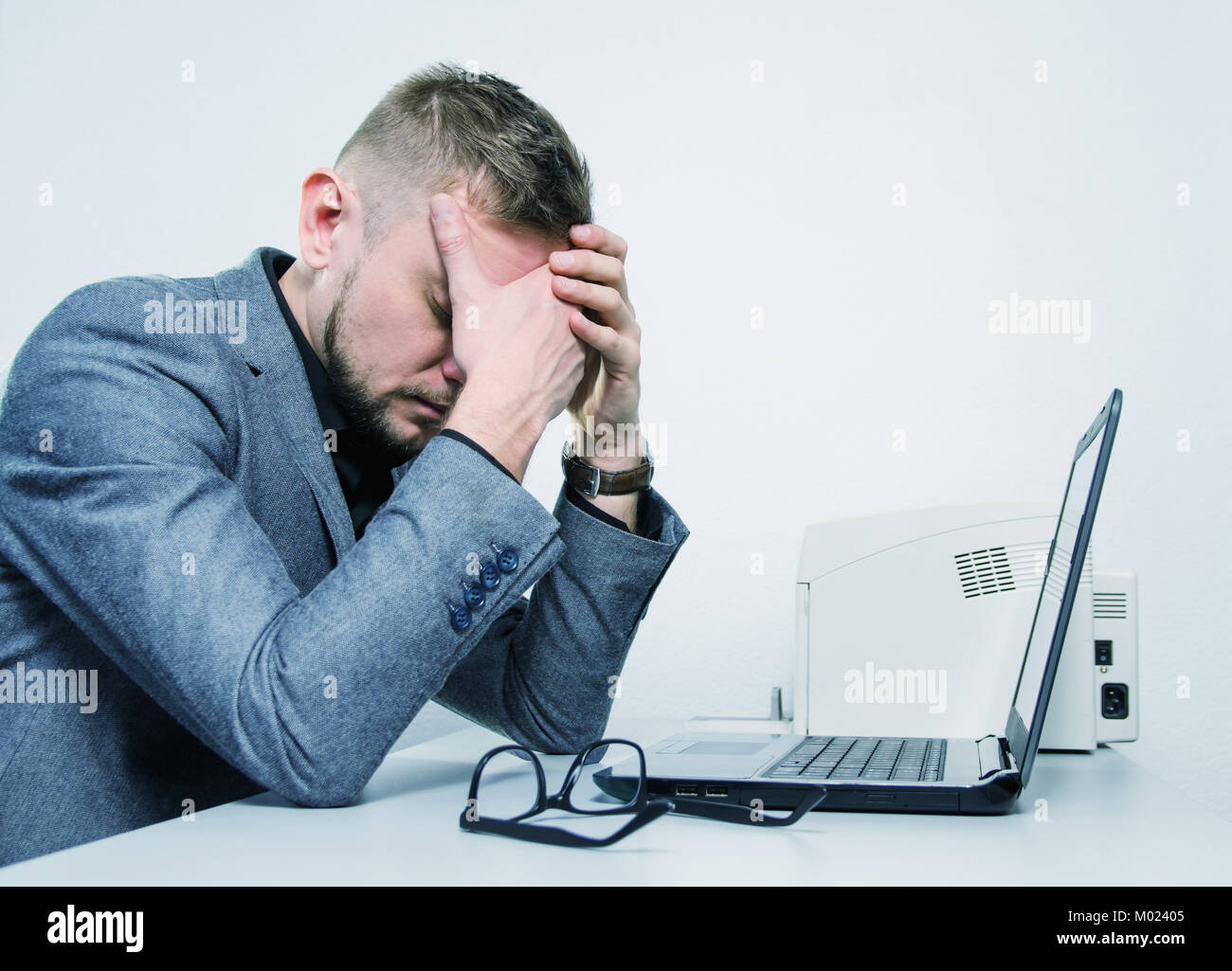 a tired man with his hands on the his face at the table with a laptop in the office. toned. Stock Photo
