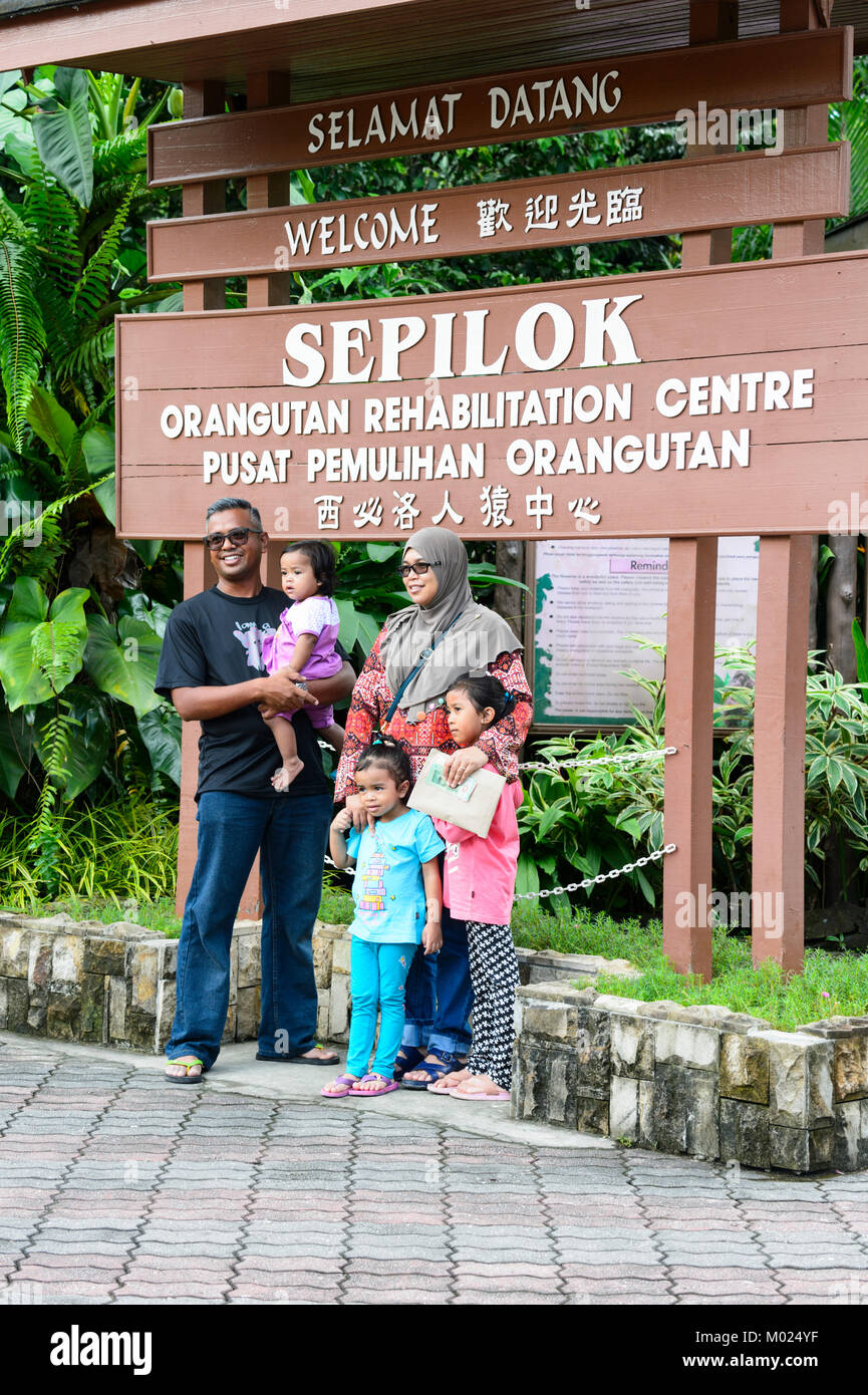 Malaysian family posing in front of the Sepilok Orangutan Rehabilitation Centre, Borneo, Sabah, Malaysia Stock Photo