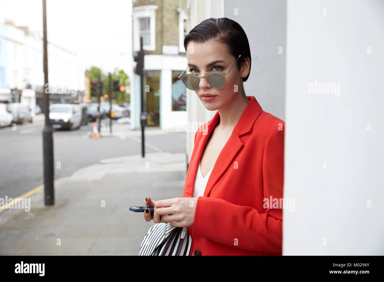 Woman in red jacket on the street, looking over sunglasses Stock Photo