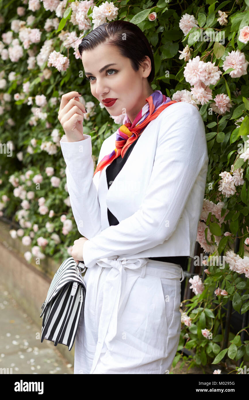 Woman in white linen suit standing by flower bush, side view Stock Photo