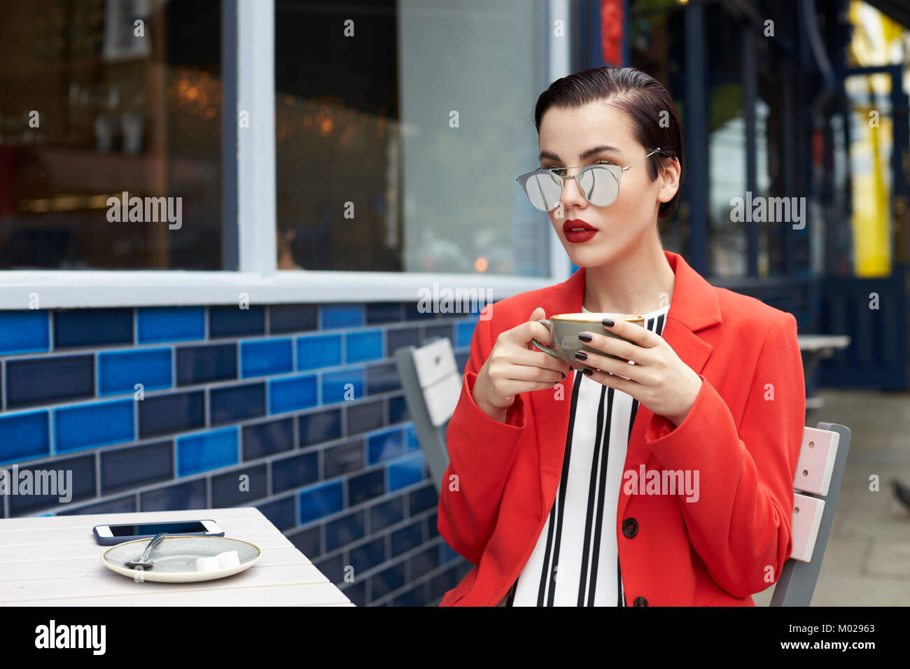 Woman in red jacket sitting outside a cafe, waist up Stock Photo