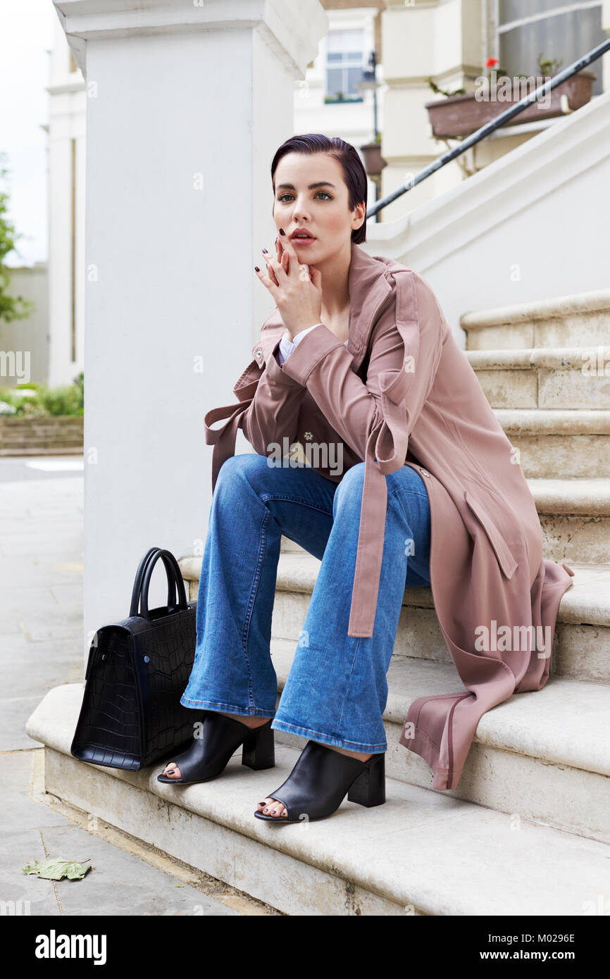Woman in coat and jeans sitting on steps outside a house Stock Photo