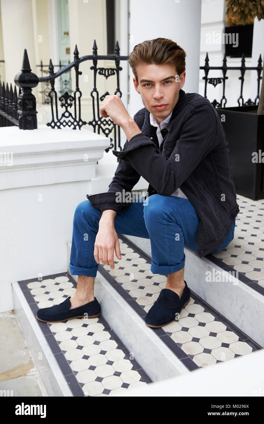 Young man sitting on steps outside a house looking to camera Stock Photo