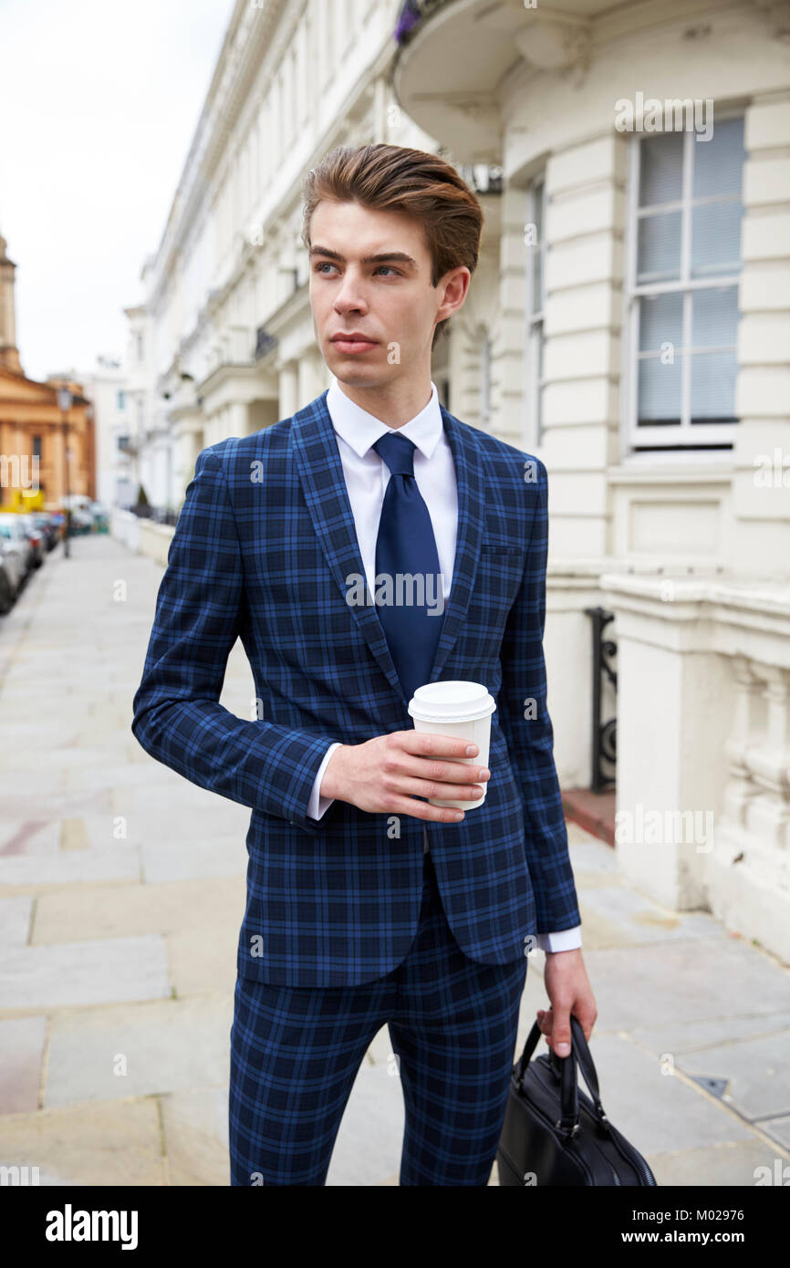 Young man in blue check suit standing in street with coffee Stock Photo
