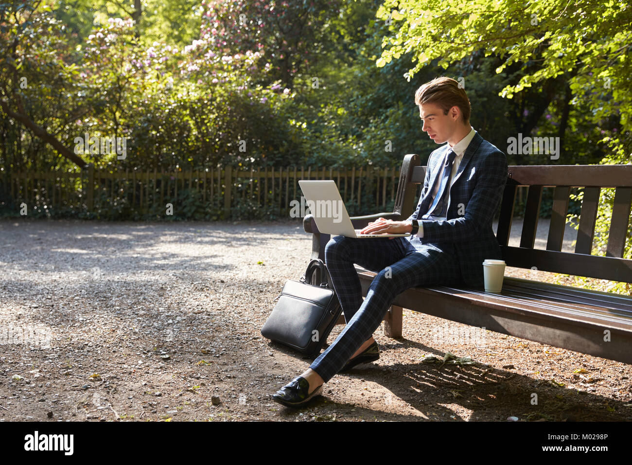 Young businessman using laptop on park bench Stock Photo