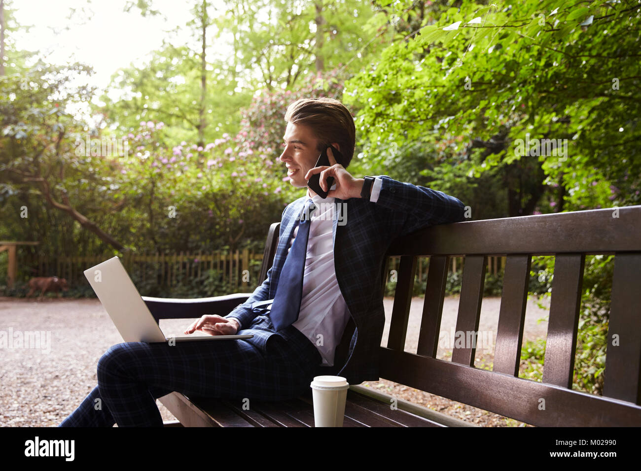 Young businessman sitting on bench using laptop and phone Stock Photo
