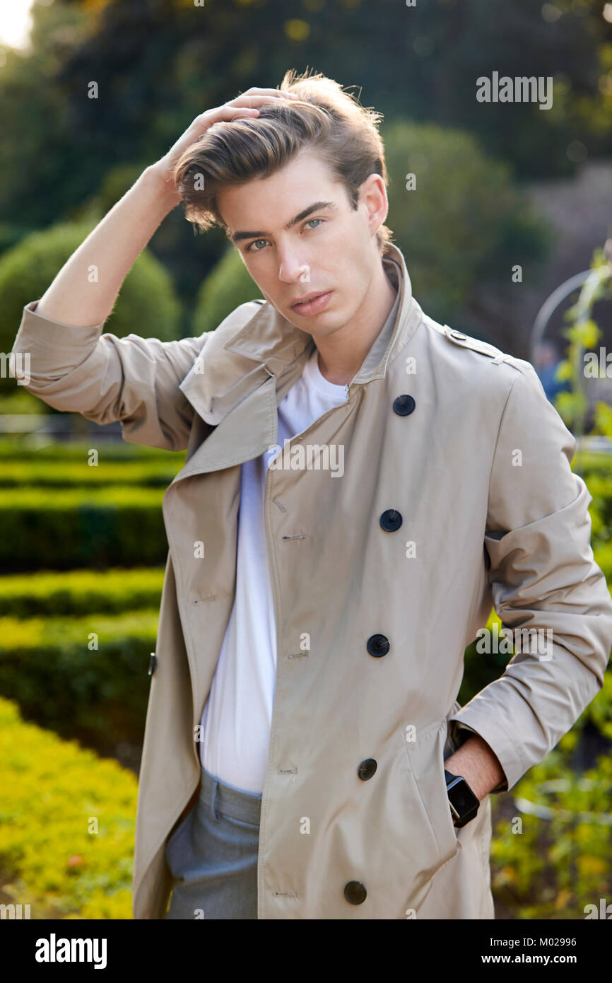 Fashionable young man in short beige macintosh in park Stock Photo