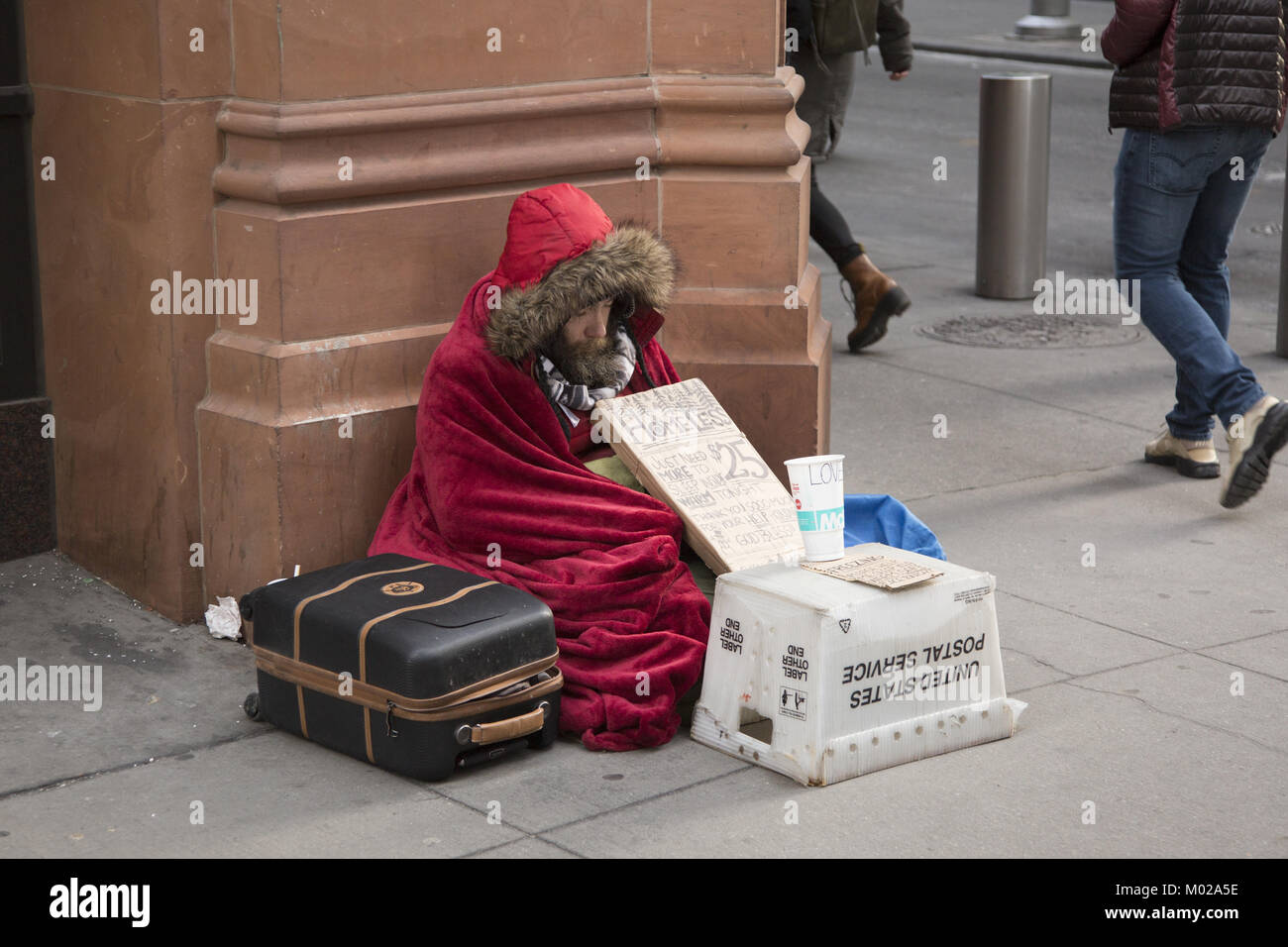 Homeless man sits bundled up on a very cold winter day asking for help  in the Financial District in Lower Manhattan, NYC. Stock Photo