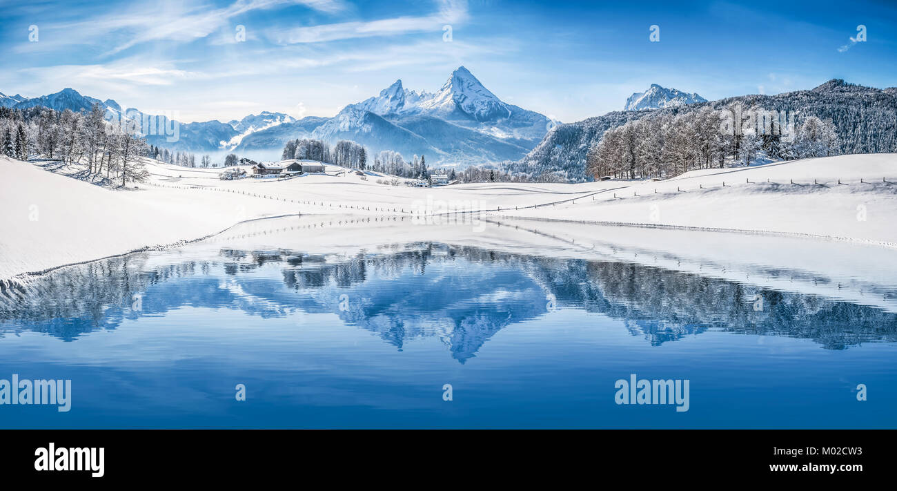 Panoramic view of beautiful white winter wonderland scenery in the Alps with snowy mountain summits reflecting in crystal clear mountain lake Stock Photo