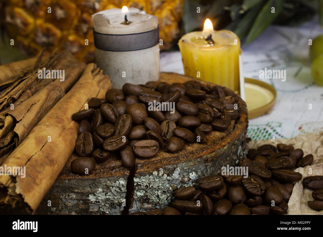 a cosy scene of coffee beans on rustic wood, one candle and sticks of cinnamon Stock Photo