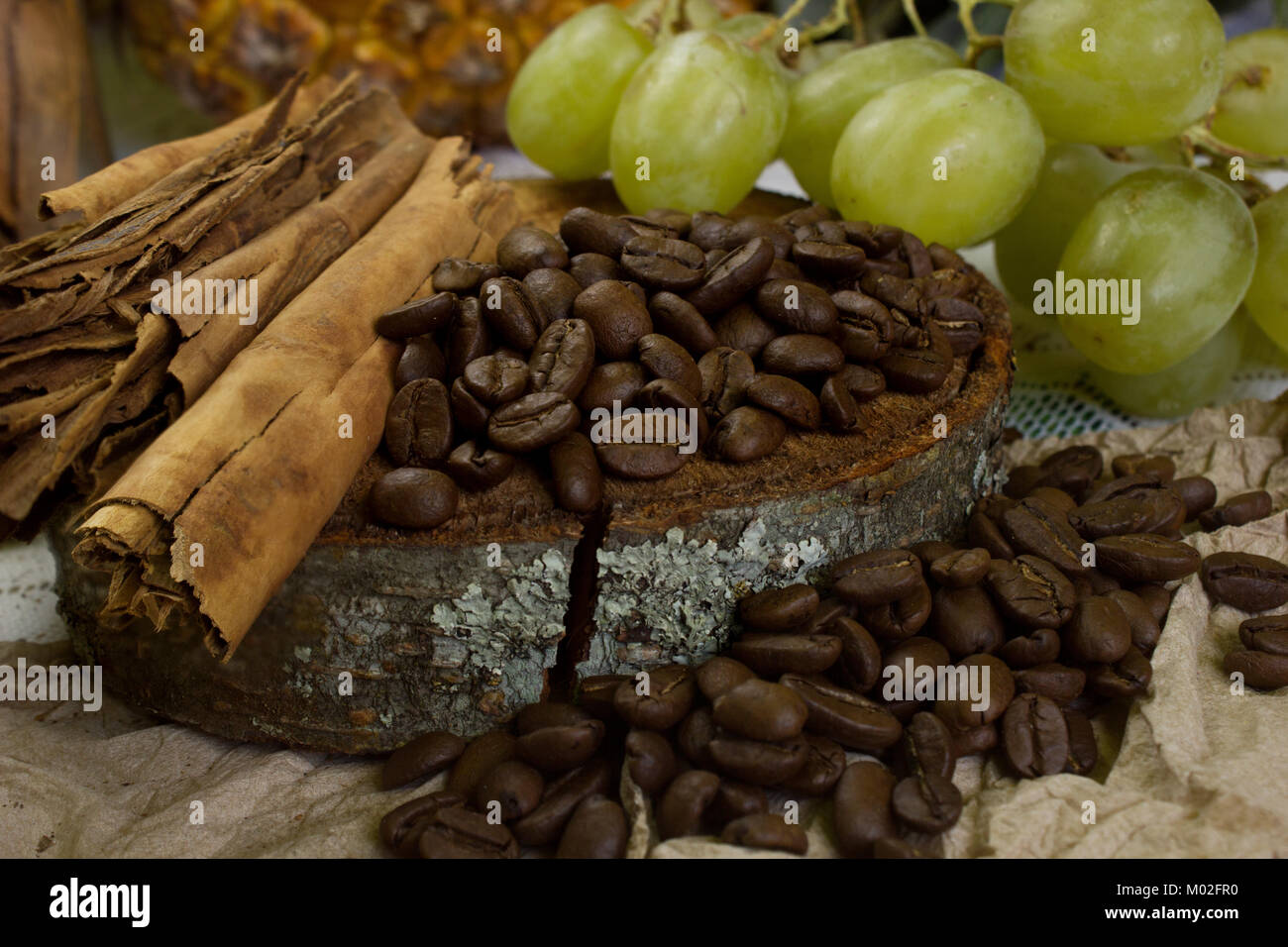 a cosy scene of coffee beans on rustic wood, sticks of cinnamon and grapes Stock Photo