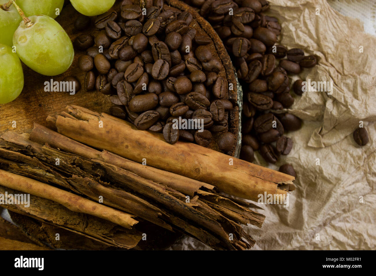 top view of a cosy scene of coffee beans on rustic wood, sticks of cinnamon and grapes Stock Photo