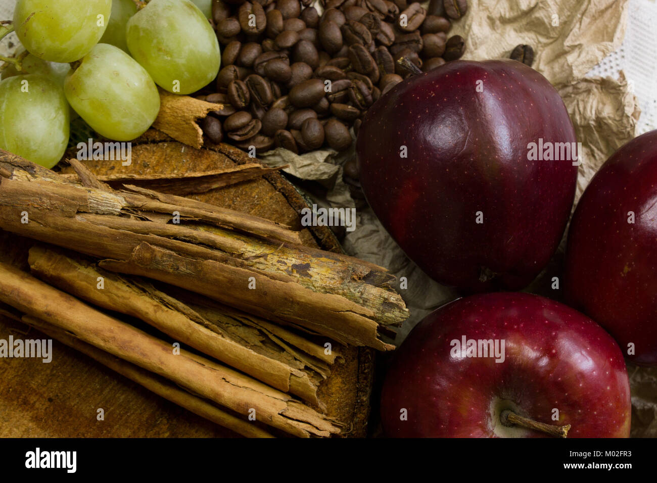 top view of a cosy scene of coffee beans on rustic wood, sticks of cinnamon, red apples and grapes Stock Photo
