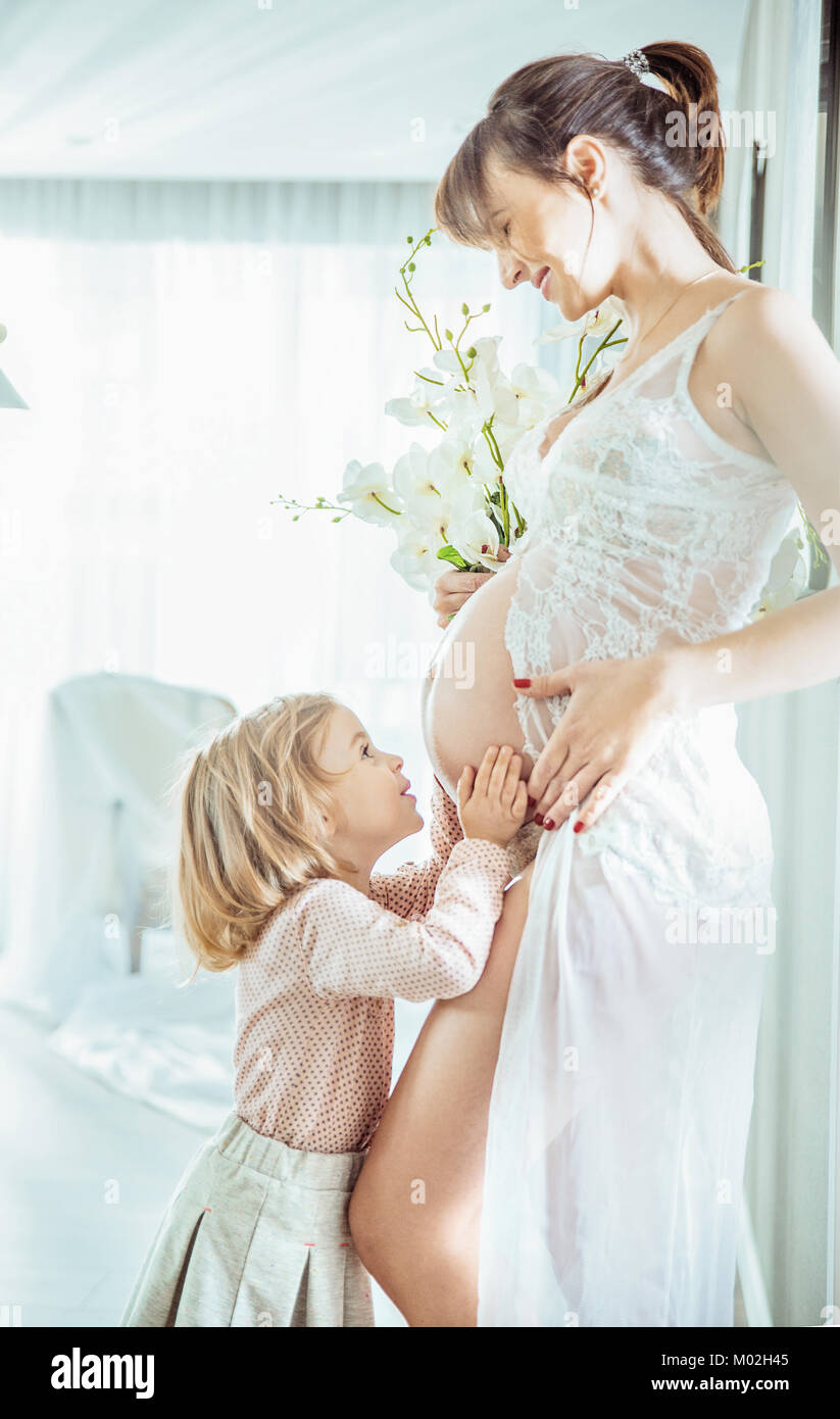 Cheerful daughter hugging pregnant mother's belly Stock Photo