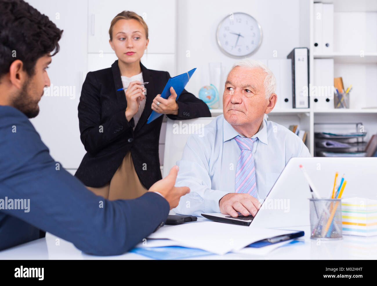 Mature male is talking to colleague, while the secretary writing ...