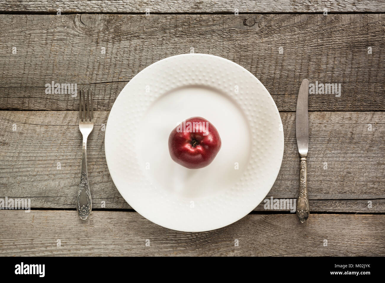 Table setting with red apple on white plate with knife and fork. Stock Photo