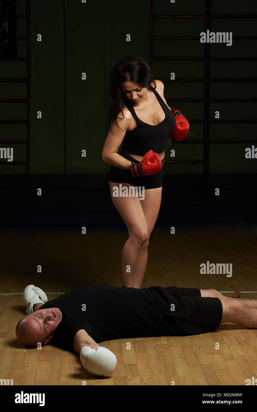 Woman knockout man in boxing pose. Woman looking on floor laying male boxer Stock Photo
