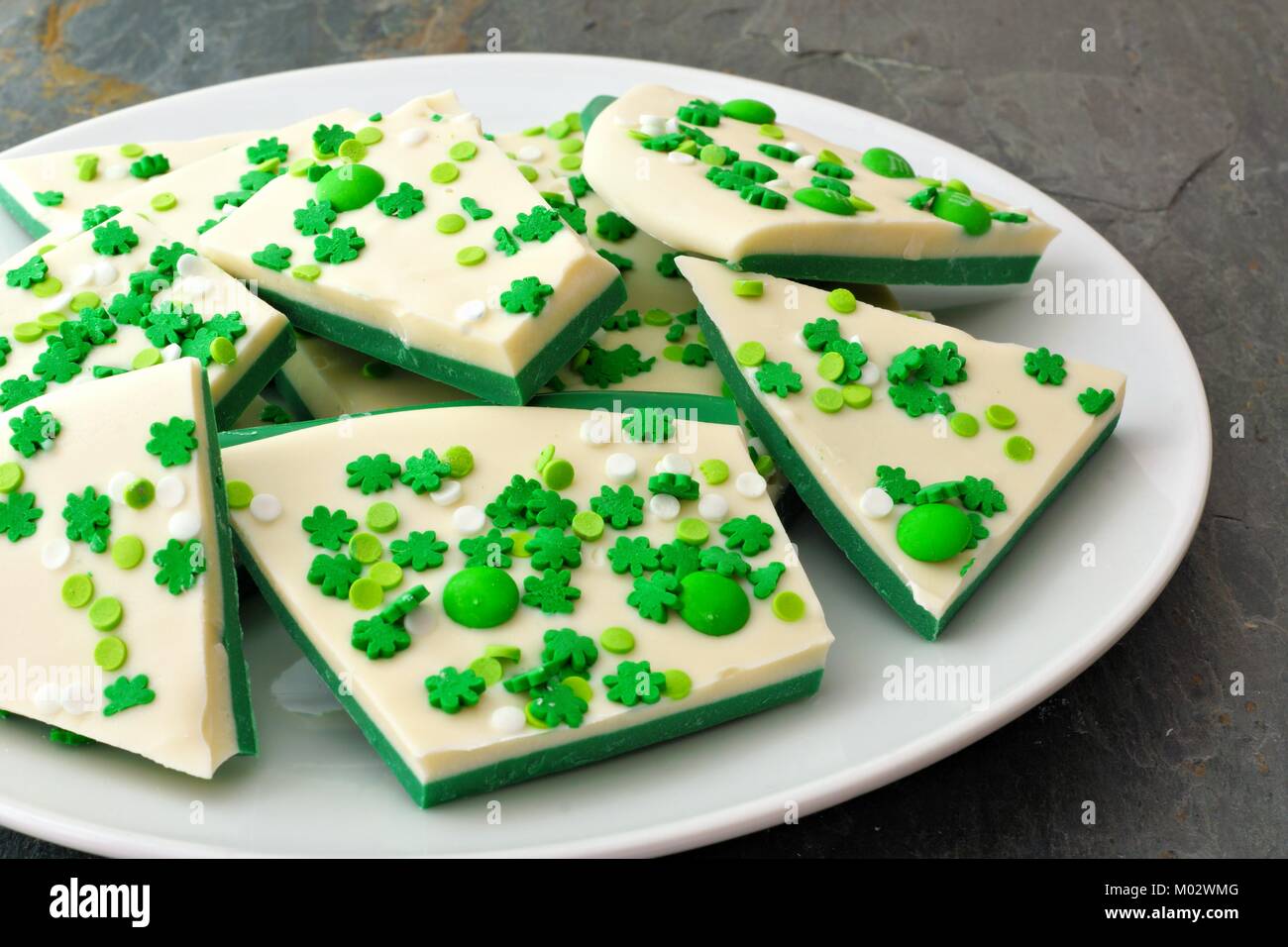 Plate of St Patricks Day chocolate candy bark with shamrock sprinkles over a slate background Stock Photo