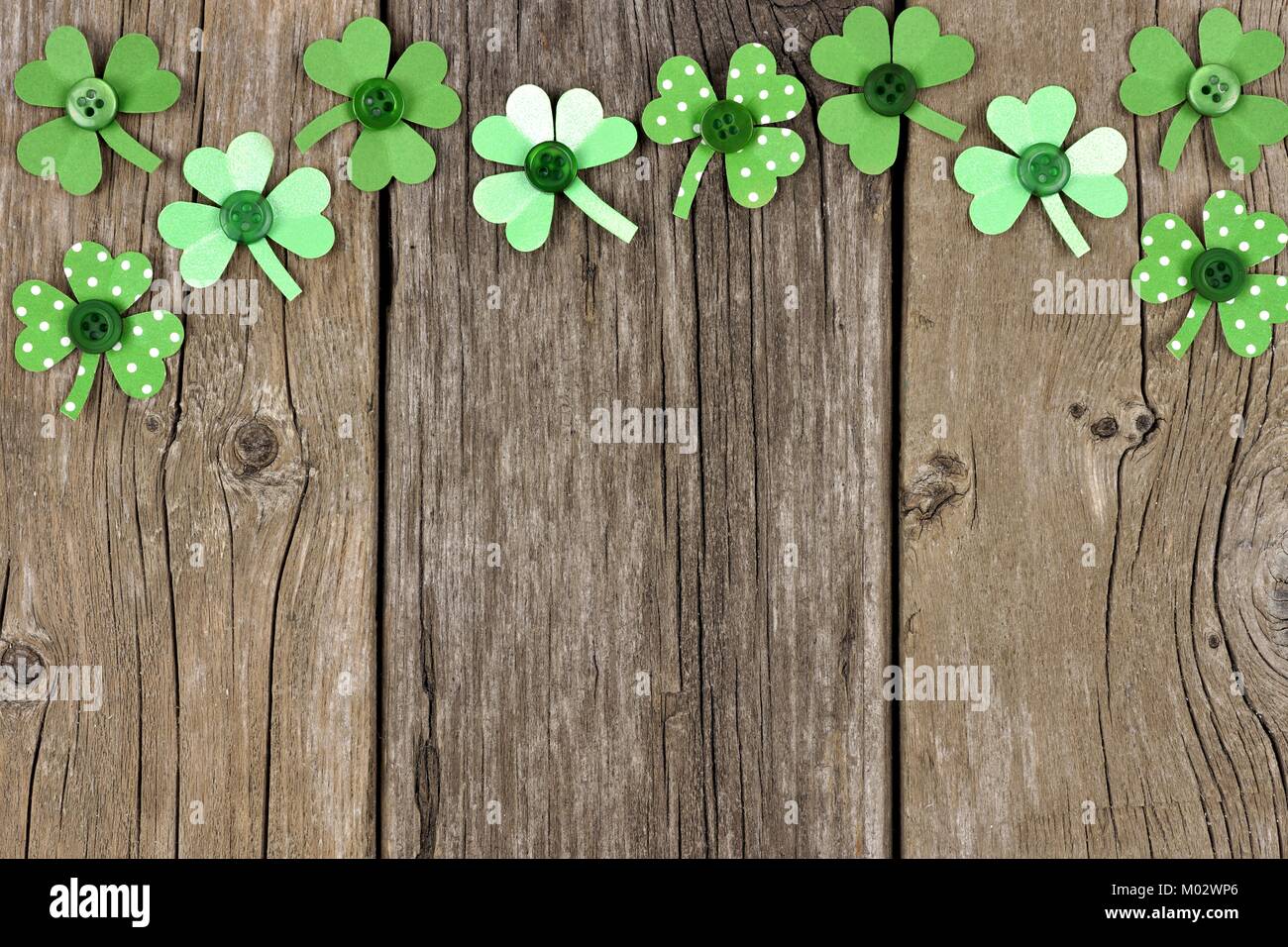 St Patricks Day top border of handmade paper shamrocks over a rustic wood background Stock Photo