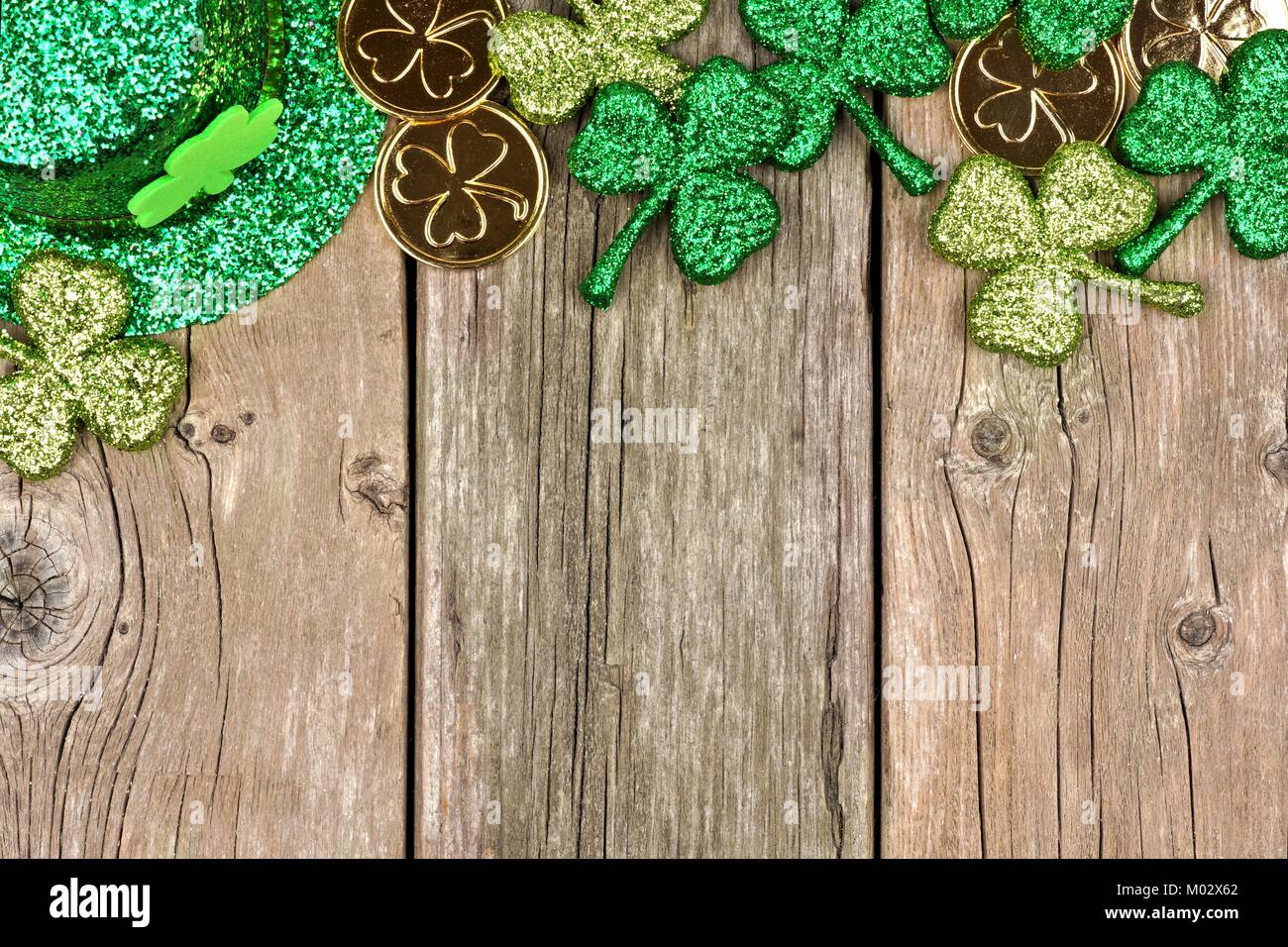 St Patricks Day top border of shamrocks, gold coins and leprechaun hat over rustic wood Stock Photo