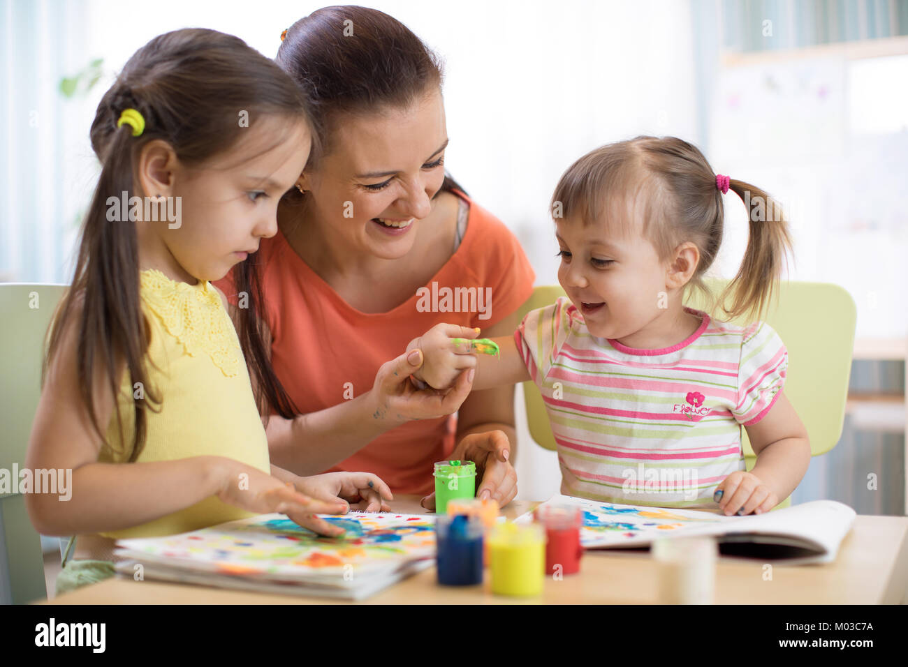 Mother and children draws with colored paints. Games with child affect early kids development. Stock Photo