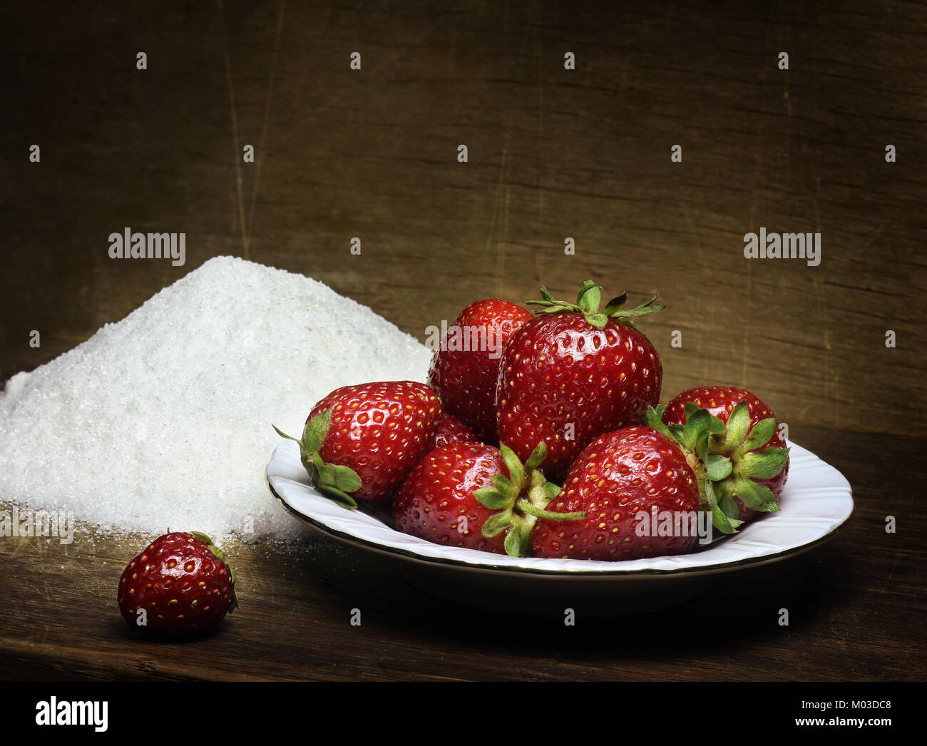 A dish with fresh strawberries and heap of sugar on a wooden table ...