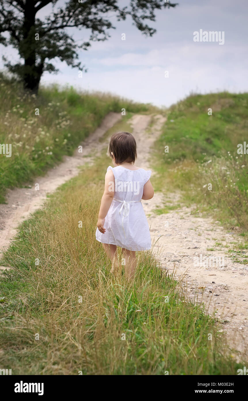 little girl walks barefoot along the road white dress and barefoot road ...