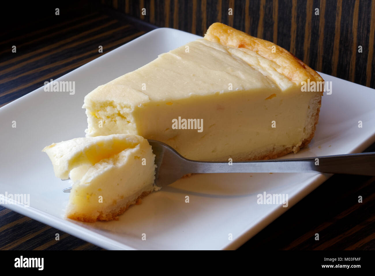 Plain baked cheesecake with cake on fork on white ceramic plate. Brown background. Stock Photo
