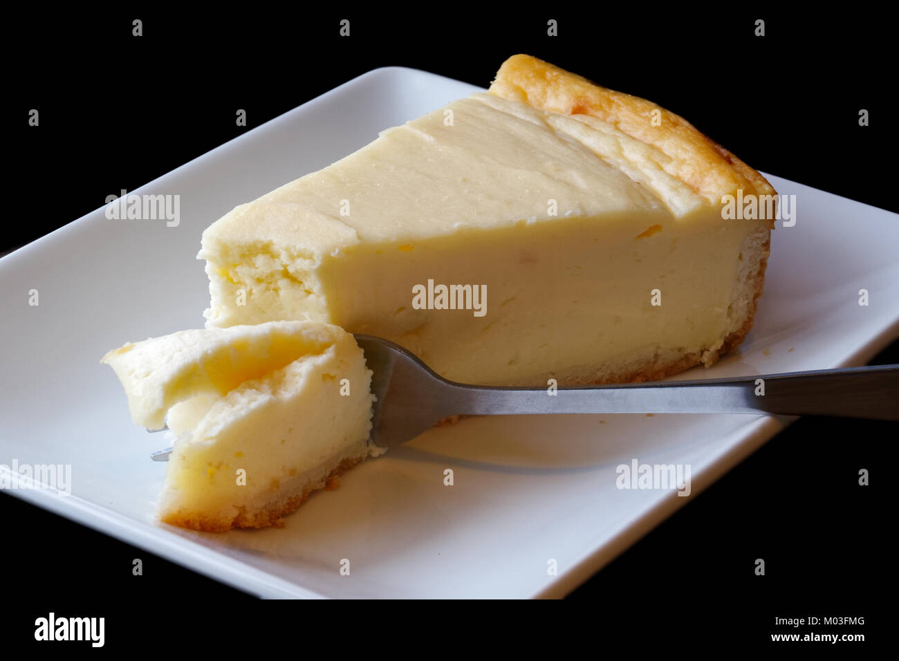 Plain baked cheesecake with cake on fork on white ceramic plate. Black background. Stock Photo