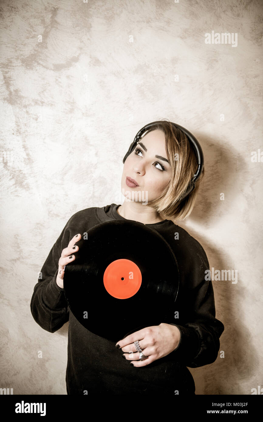 Young blond pretty woman with headphones looking up with vintage vinyl record long playing in her hands Stock Photo