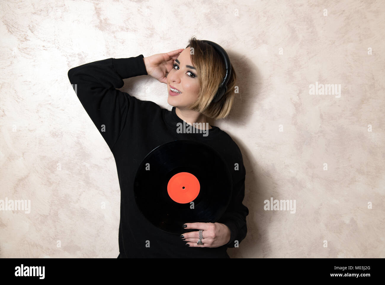 Young blond pretty woman with headphones looking at camera with vintage vinyl record long playing in her hands Stock Photo