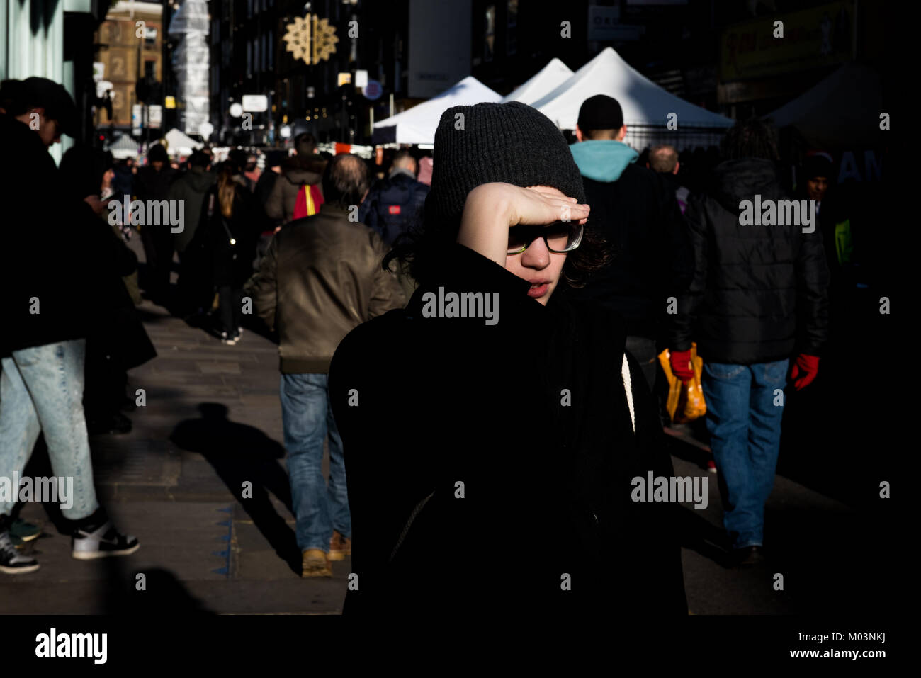 A person shields their eyes from the low sun at Londons Brick Lane Market, Bethnal Green. Stock Photo
