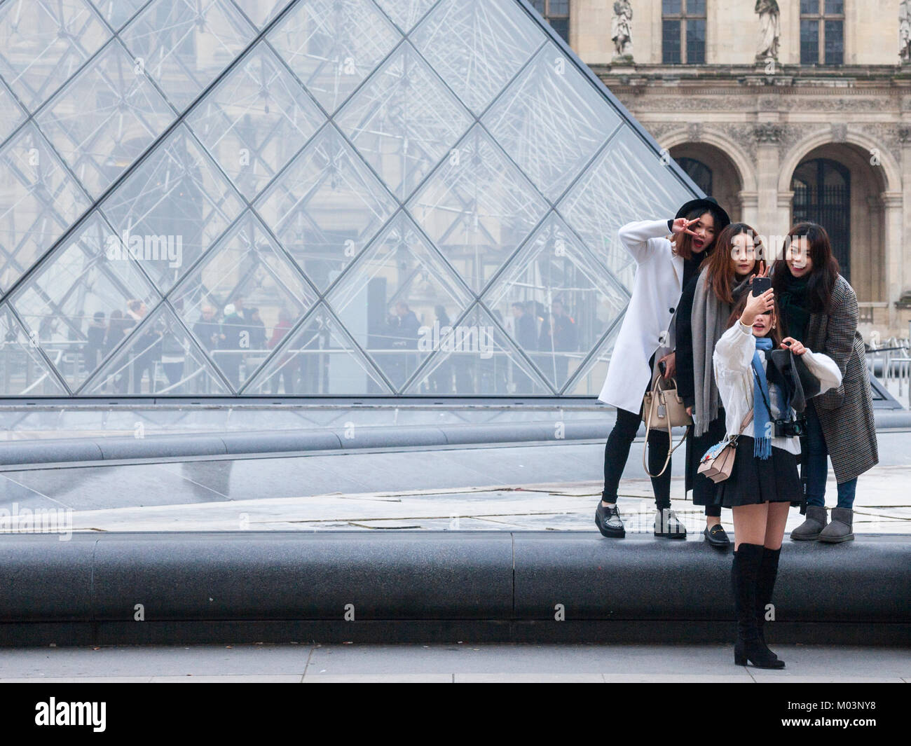PARIS, FRANCE - DECEMBER 20, 2017: Chinese tourists taking selfie photos in front of the Louvre Pyramid. Louvre pyramid (Pyramide du Louvre) is one of Stock Photo