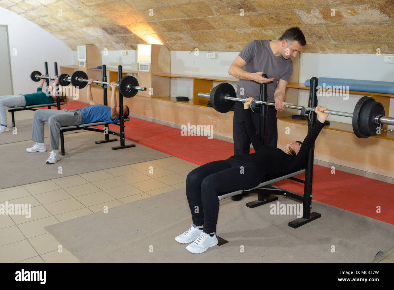 personal male trainer helping young woman with lifting barbell Stock ...