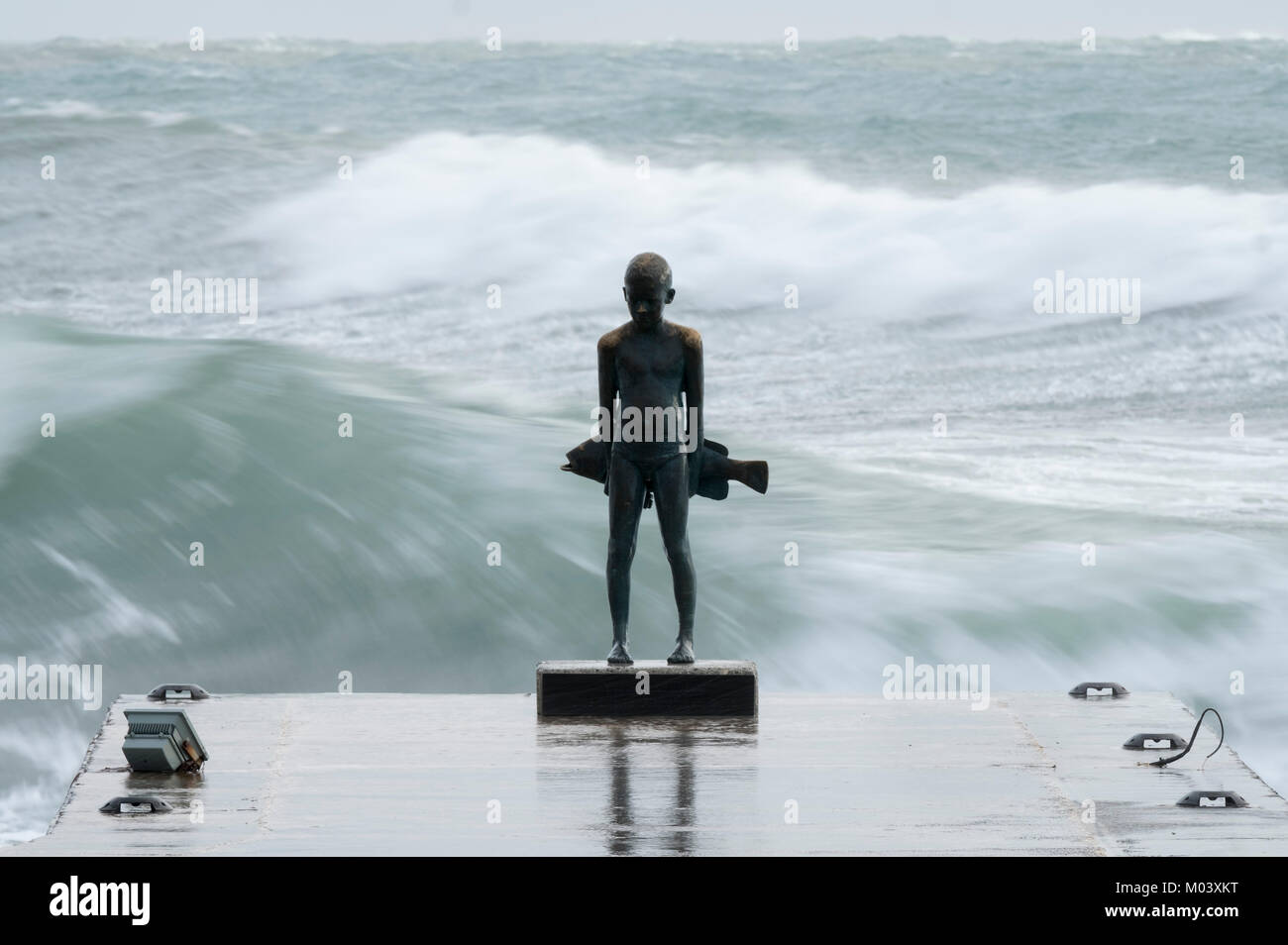 Paphos, Cyprus. 18th Jan, 2018. The little fisherman”- a bronze of a young boy and a large fish by Paphos artist, Yiota Ioannidou is battered by large waves in Paphos harbour, Republic of Cyprus. Picture Credit: Ian Rutherford/Alamy Live News Stock Photo