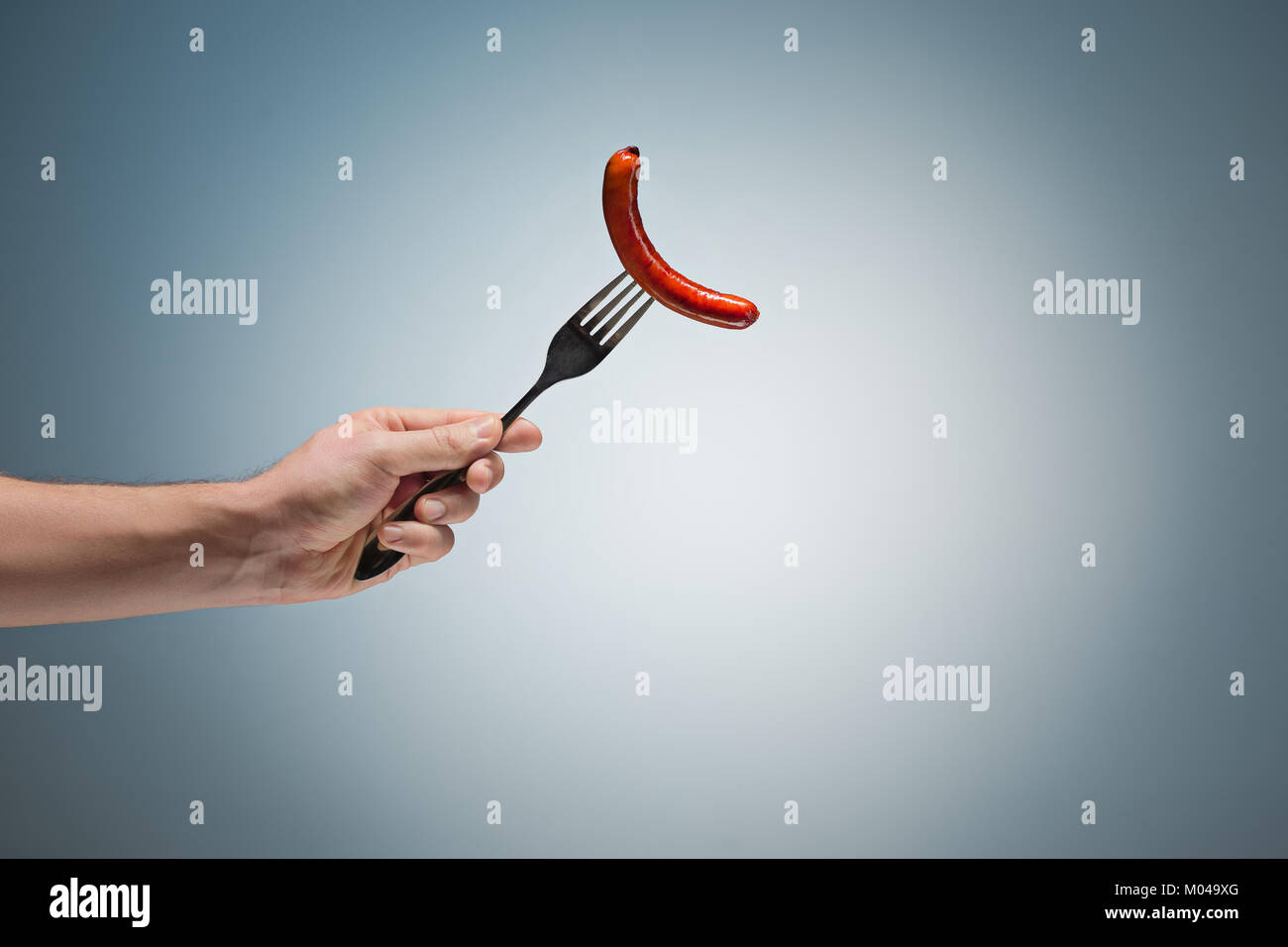 sausage on a fork in his hand Stock Photo