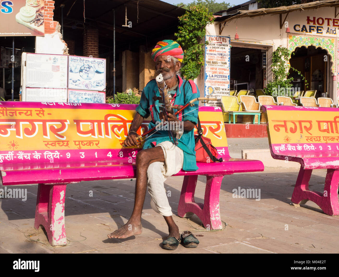A colorful photograph of an old Indian  street musician holding his  music instruments wearing a rainbow colored hat. Stock Photo