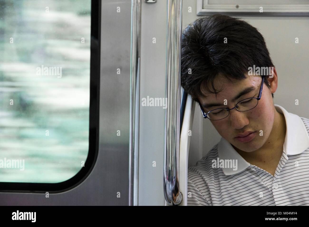 Young Japanese male student sleeping inside a train in Tokyo, Japan, close to a window Stock Photo