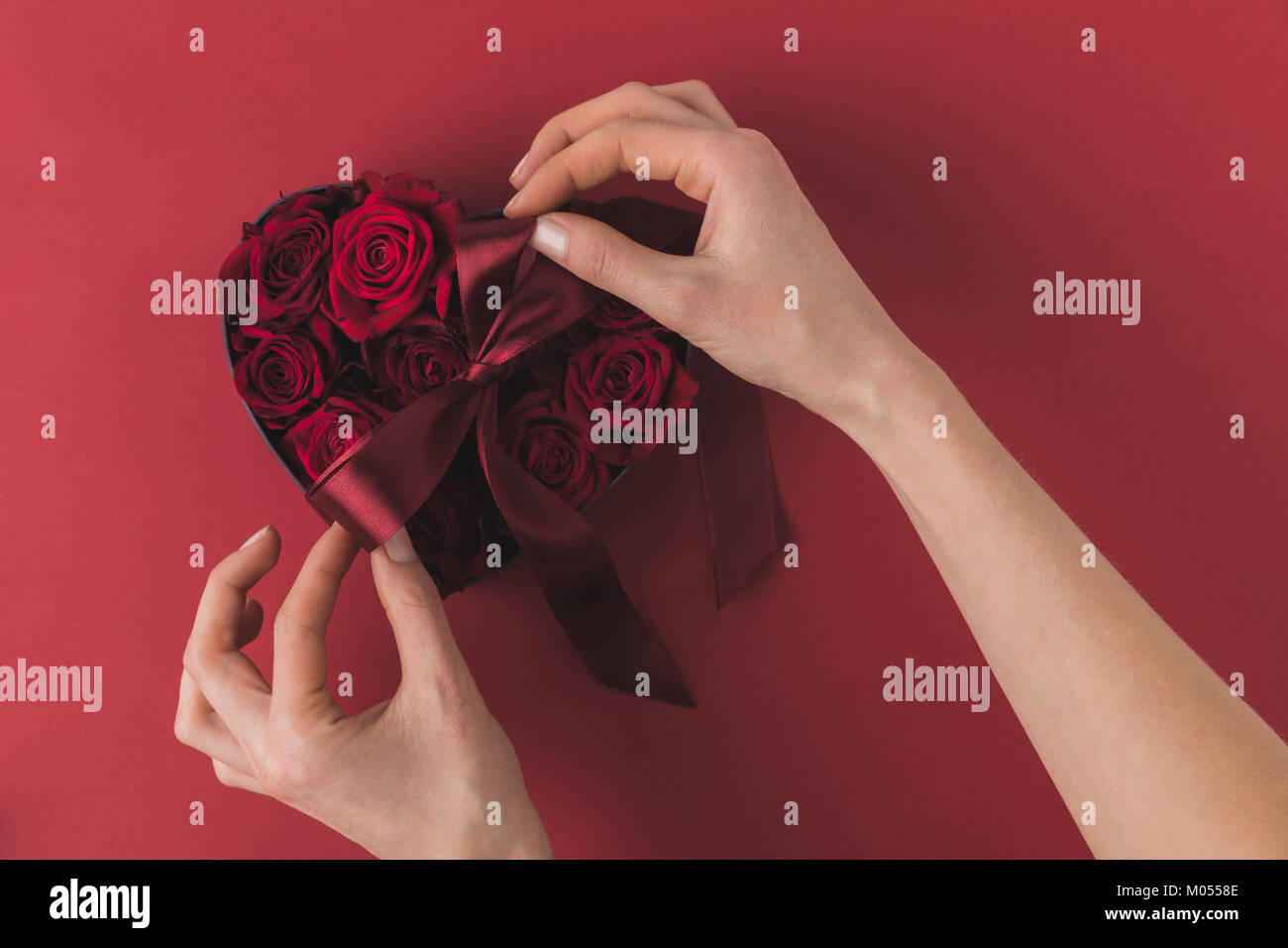 partial view of woman tying ribbon on heart shaped box with roses on