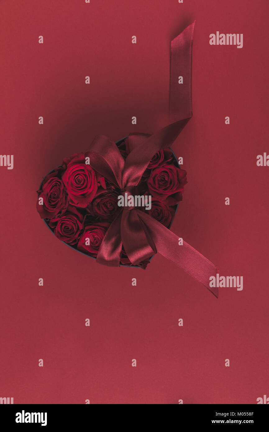 top view of roses in heart shaped gift box with ribbon isolated on red ...