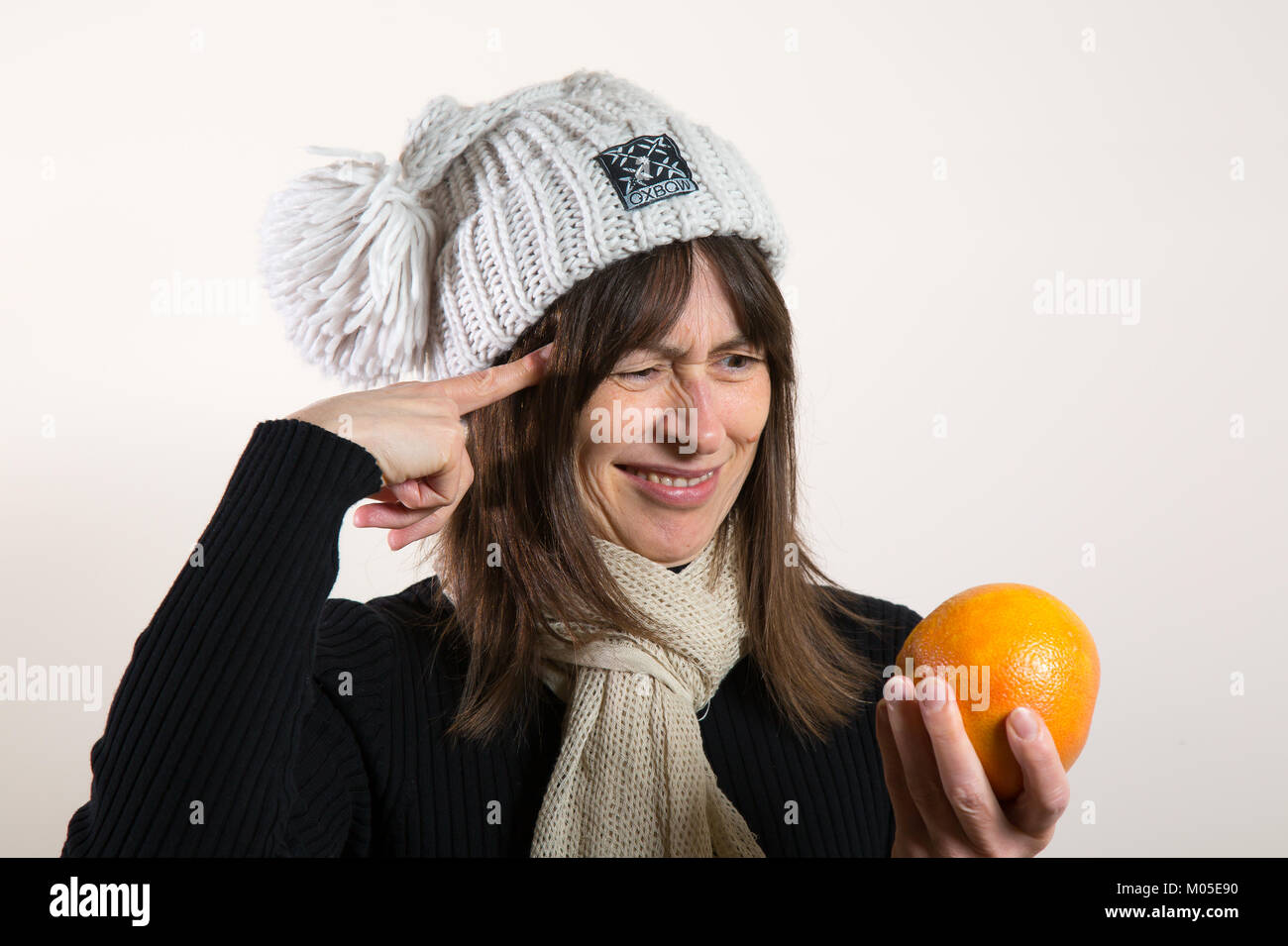 Dilemma, question: small grapefruit or big orange? Young lady puzzled about fresh fruit in her hand. Stock Photo