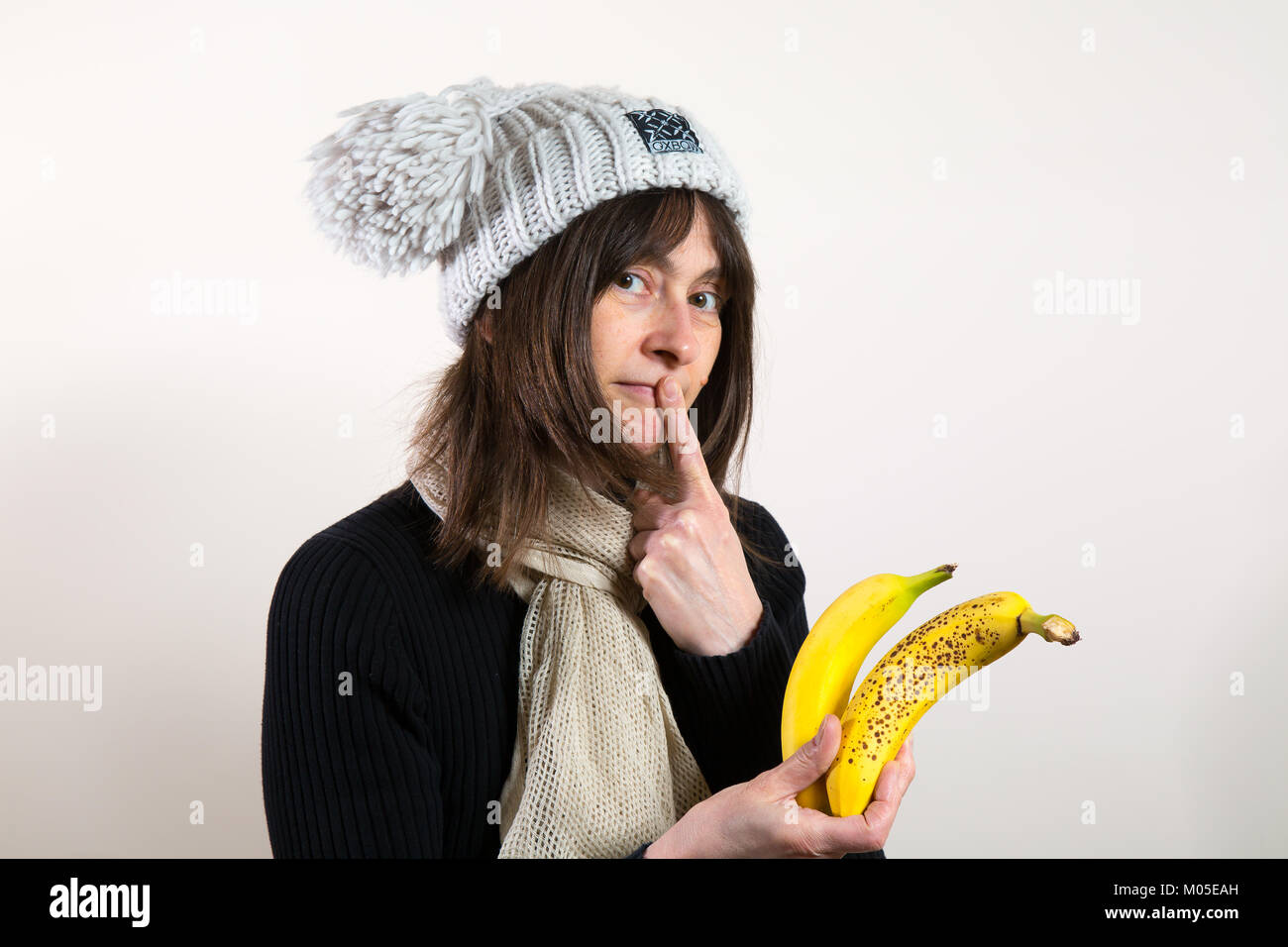 Portrait of attractive female trying to decide to eat ripe banana or unripe banana. Healthy eating & making your mind up. Stock Photo