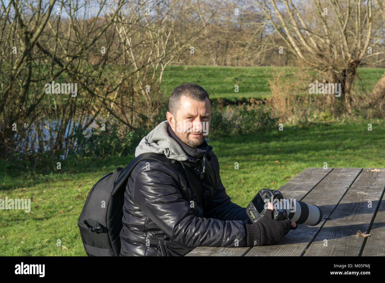 Professional nature photographer rests his Canon camera on picnic table & takes a break from taking pictures in the park on a cold winter morning. Stock Photo