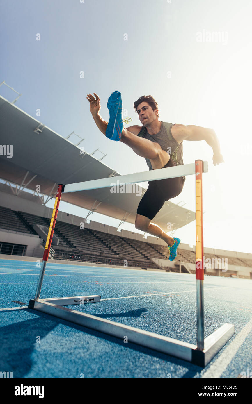 Runner jumping over an hurdle during track and field event. Athlete running a hurdle race in a stadium. Stock Photo