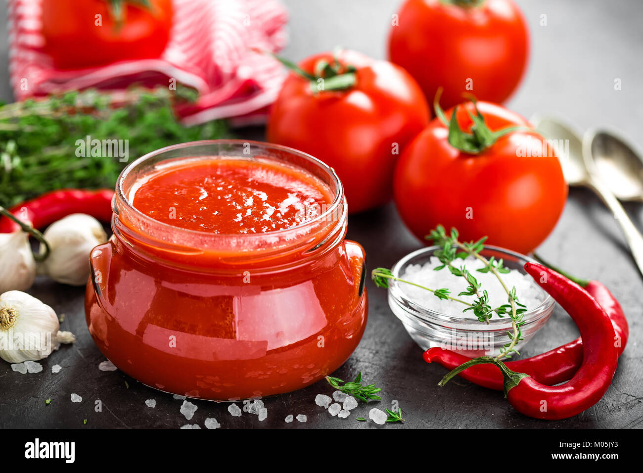 Tomato paste, puree in glass jar and fresh tomatos on dark background