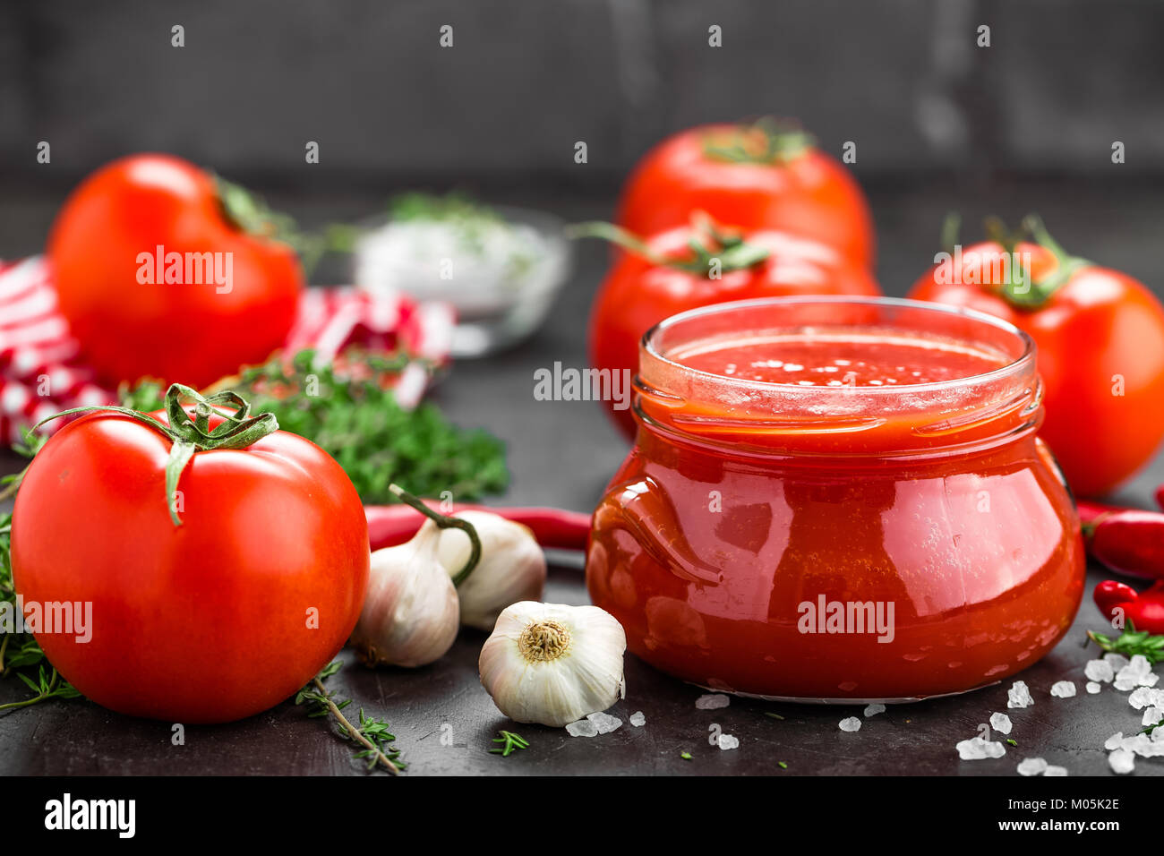 Tomato paste, puree in glass jar and fresh tomatos on dark background