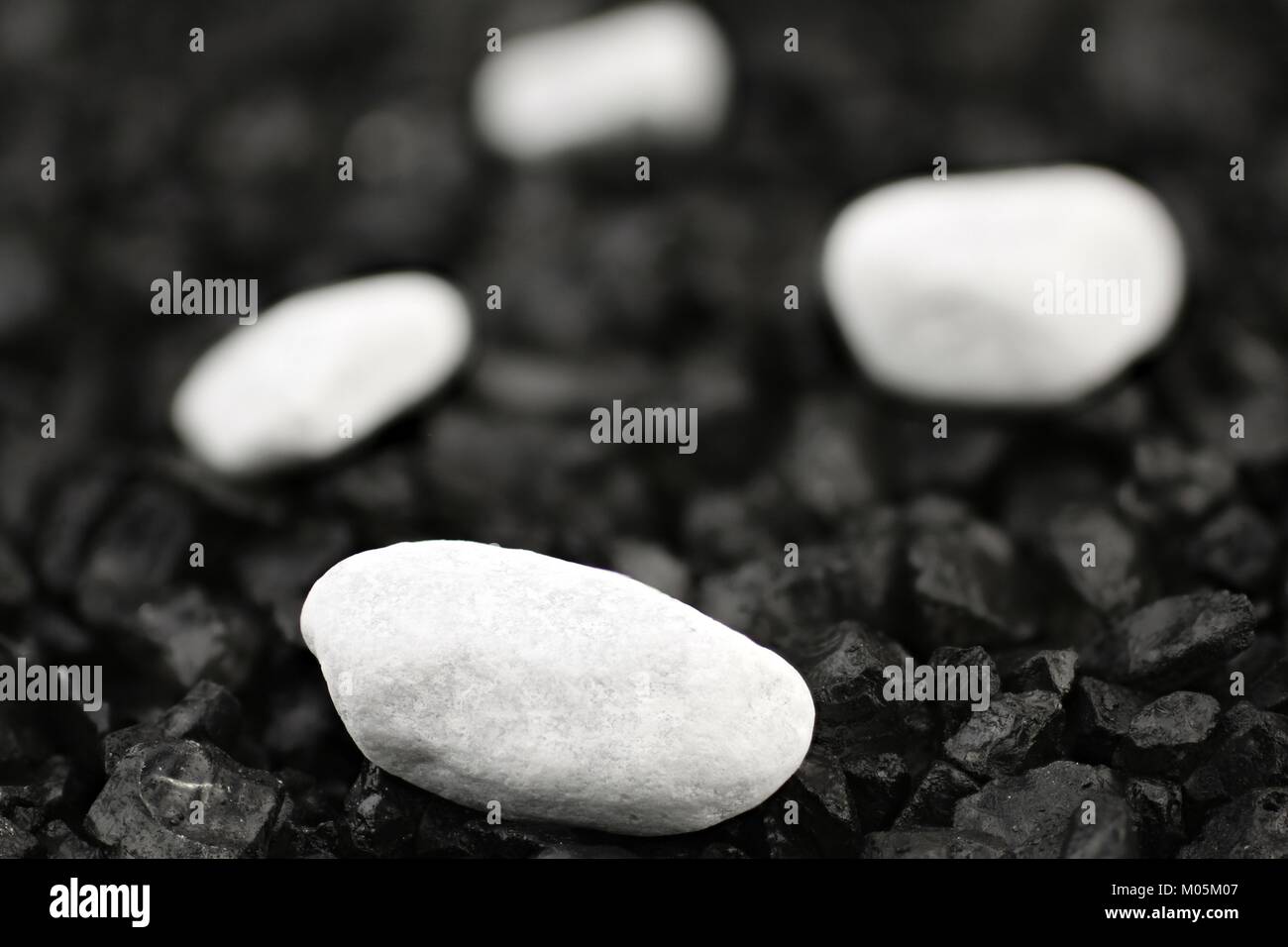 White pebbles in front of black background with black grit Stock Photo