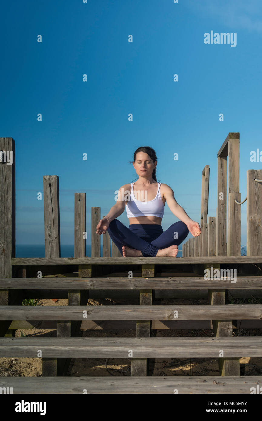 woman meditating in the lotus position sitting on wooden steps by the ...